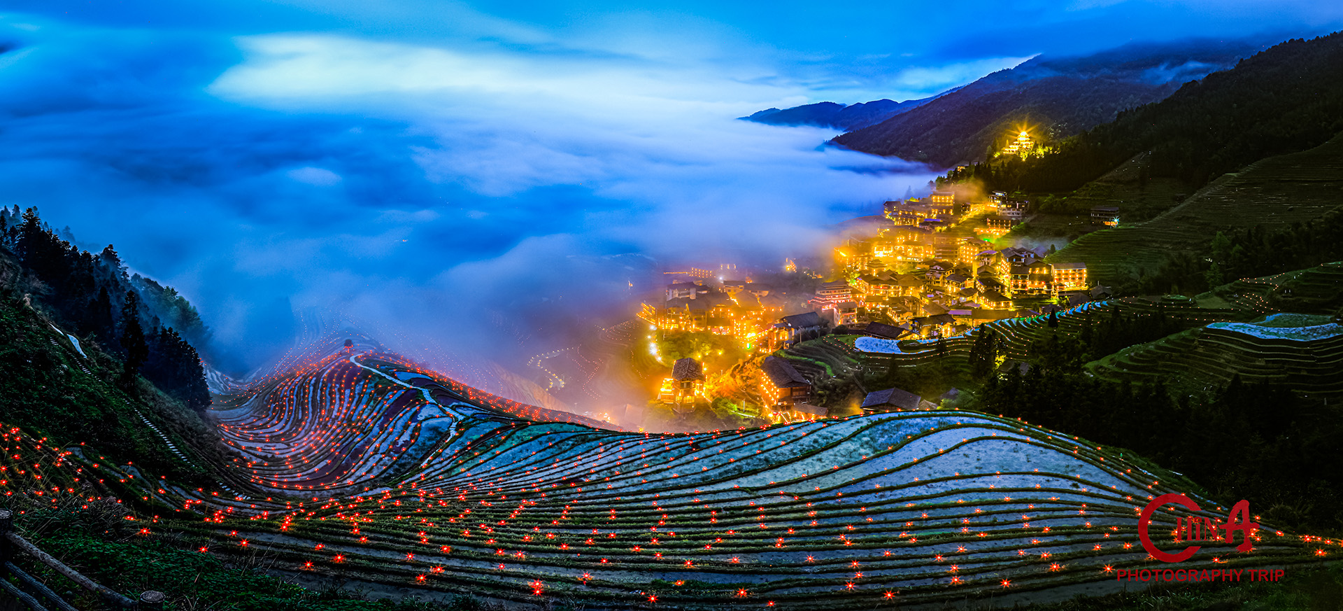 Jinkeng Dazhai at blue hour — lamp-lit terraces below the Yao village, cloud spilling over the ridge
