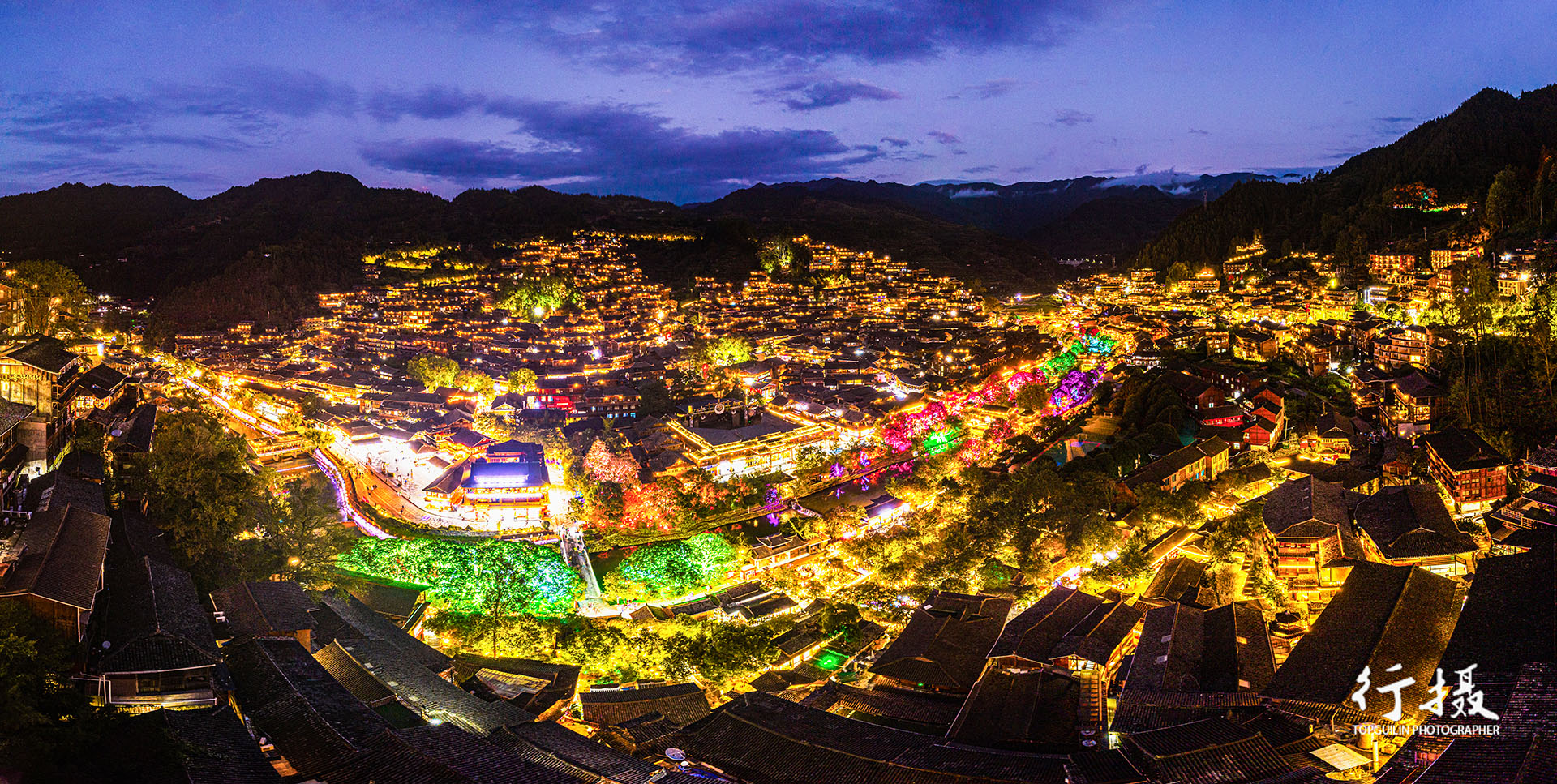 Xijiang Qianhu Miao Village at blue hour, thousands of stilt houses lit across both slopes of the valley