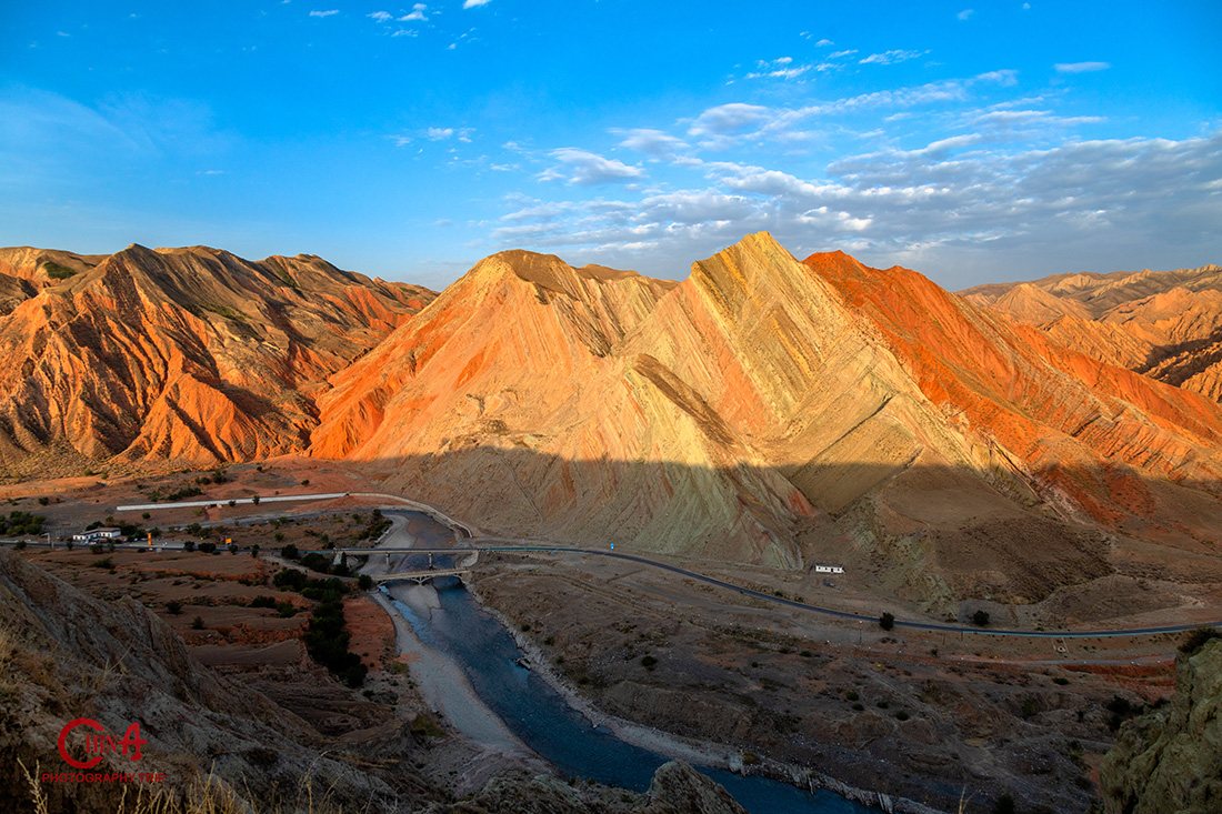 Rainbow-striped Danxia ridges above a river valley on Xinjiang's Defence Highway S101 at dawn