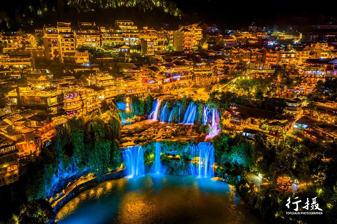 Furong Town at night with water pouring down the cliff beside lantern-lit stilt houses
